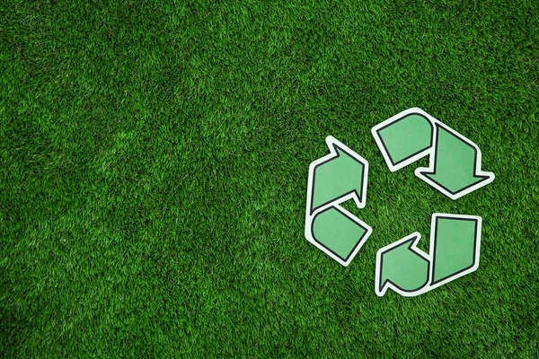 Paper recycling symbol on green grass, top view. Space for text