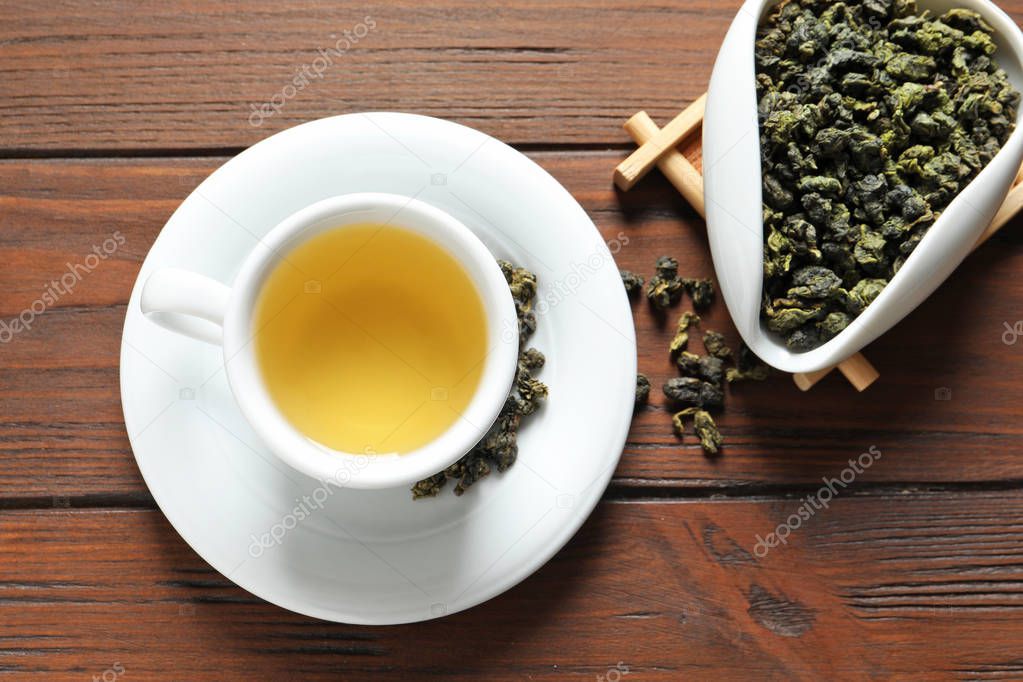 Cup of Tie Guan Yin oolong and chahe with tea leaves on wooden table, top view