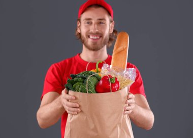 Delivery man holding paper bag with food products on dark background