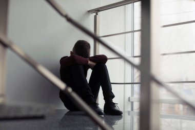 Upset preteen boy sitting on staircase indoors clipart