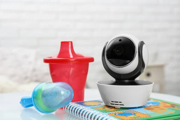 Modern CCTV security camera, baby cup, nibbler and book on table indoors — Stockfoto