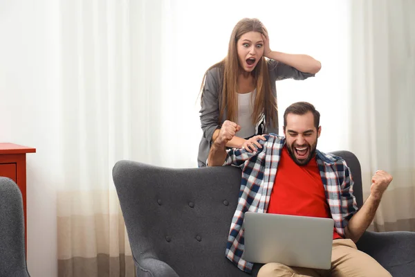 Emotional young couple with laptop celebrating victory at home