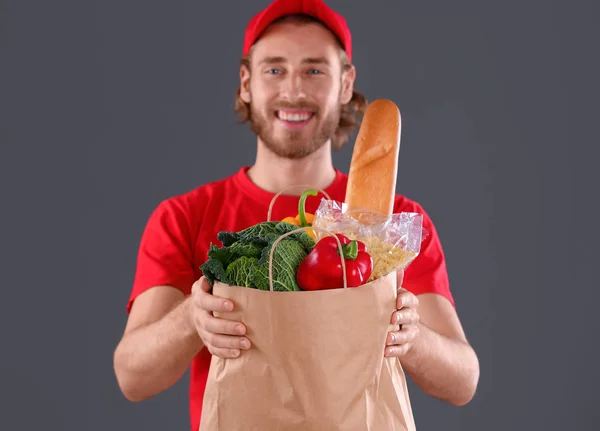 Livraison homme tenant sac en papier avec des produits alimentaires sur fond sombre — Photo