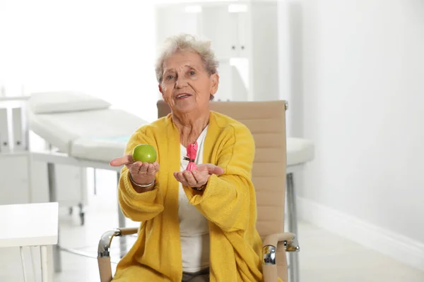 Mujer mayor con entre manzana y caramelo en el hospital. Dieta diabética —  Fotos de Stock