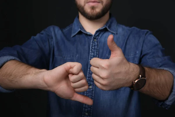 Homme montrant THUMB UP et DOWN geste en langue des signes sur fond noir, gros plan — Photo