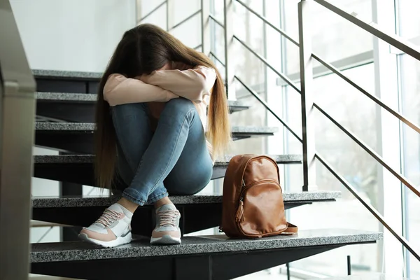 Menina adolescente perturbada com mochila sentada nas escadas dentro de casa — Fotografia de Stock