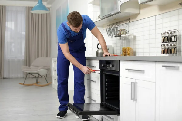 Professional serviceman repairing modern oven in kitchen — Stock Photo, Image