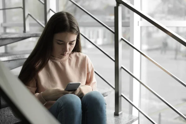 Menina adolescente perturbado com smartphone sentado em escadas dentro de casa. Espaço para texto — Fotografia de Stock