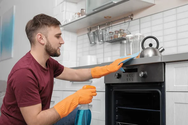 Fiatal férfi takarítás sütő rongyot és mosószer a konyhában — Stock Fotó