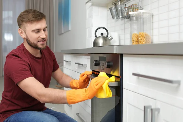 Joven limpieza horno con trapo en la cocina — Foto de Stock