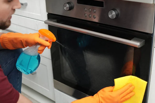 Anak muda membersihkan oven dengan kain dan deterjen di dapur, closeup — Stok Foto