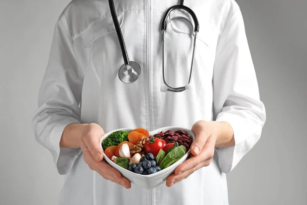 Arzt hält Schale mit Produkten für herzgesunde Ernährung auf farbigem Hintergrund, Nahaufnahme — Stockfoto