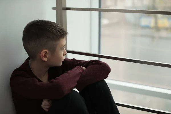 Расстроенный мальчик сидит у окна в помещении. Пространство для текста — стоковое фото