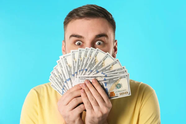 Emotional young man with money on color background — Stock Photo, Image