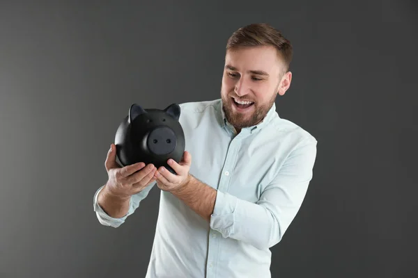 Портрет щасливого молодого чоловіка з скарбничкою на сірому фоні. Економія грошей — стокове фото
