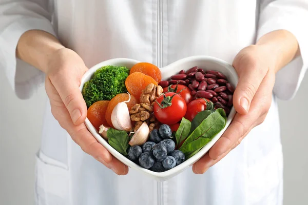 Врач держит миску с продуктами для здорового питания сердца, крупным планом — стоковое фото