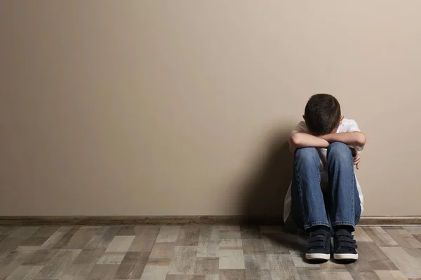 Upset boy sitting on floor at color wall. Space for text — Stock fotografie