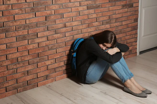 Upset teenage girl with backpack sitting on floor near wall. Space for text — Stock Photo, Image