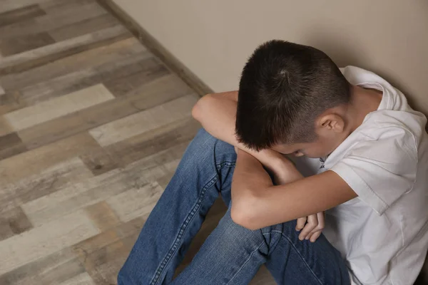 Rapaz perturbado sentado no chão, na parede. Espaço para texto — Fotografia de Stock