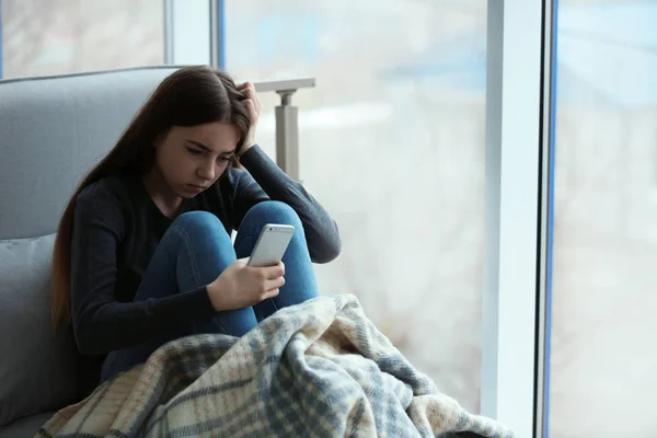 Menina adolescente perturbado com smartphone sentado na janela dentro de casa. Espaço para texto — Fotografia de Stock