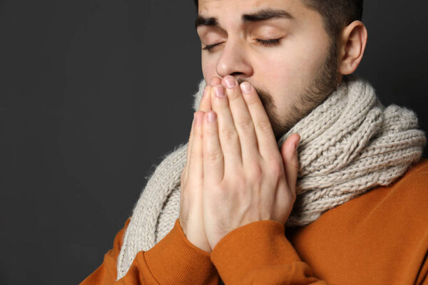 Handsome young man coughing against dark background. Space for text