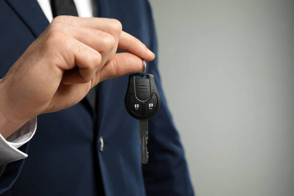 Young man holding car key on grey background, closeup. Space for text