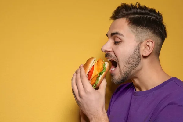 Stilig man äta välsmakande hamburgare på färgbakgrund. Utrymme för text — Stockfoto