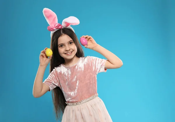 Little girl in bunny ears headband holding Easter eggs on color background, space for text — Stock Photo, Image