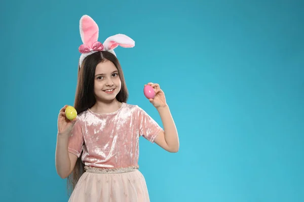 Little girl in bunny ears headband holding Easter eggs on color background, space for text — Stock Photo, Image