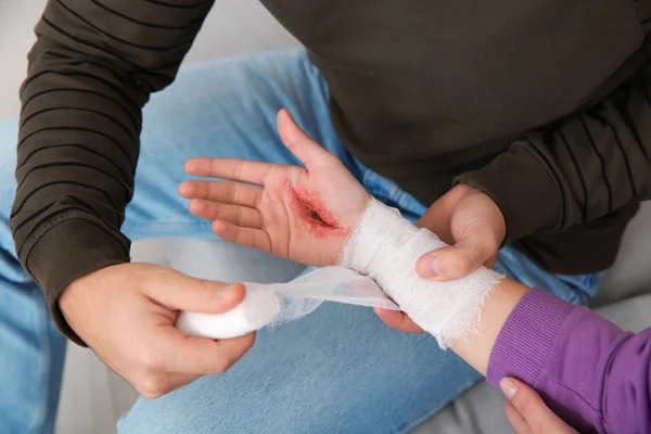 Młody człowiek stosowania bandaż na kobiety ranny ręka w domu zbliżenie. Pierwszej pomocy — Zdjęcie stockowe