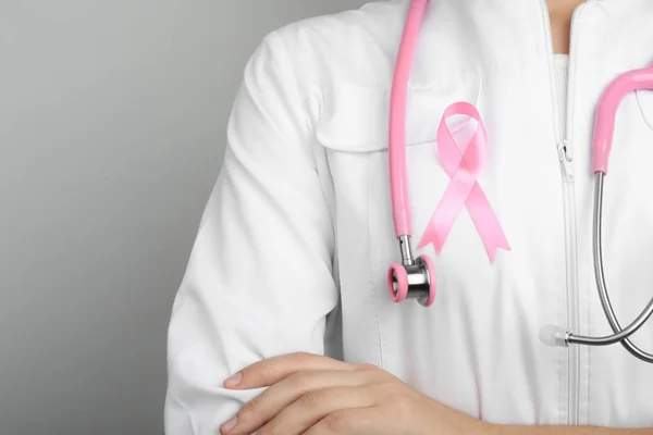 Доктор з рожевою стрічкою та стетоскопом на сірому фоні, простір для тексту. Розуміння раку молочної залози — стокове фото