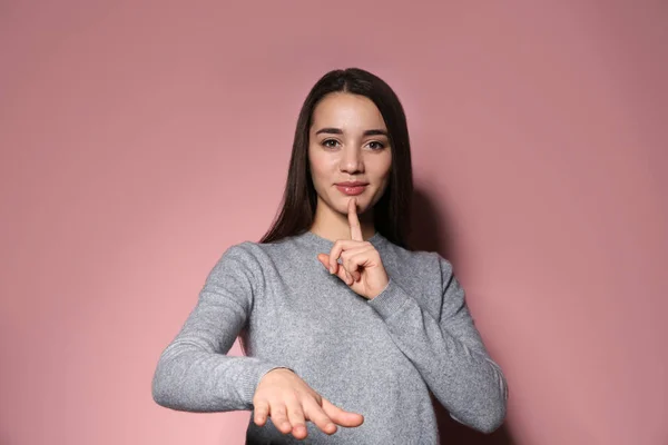 Woman showing HUSH gesture in sign language on color background — Stock Photo, Image