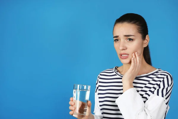 Emotionale junge Frau mit empfindlichen Zähnen und einem Glas Wasser auf farbigem Hintergrund. Raum für Text — Stockfoto