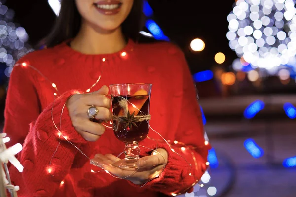 Kobieta z szklanki do grzanego wina i garland na targi, zbliżenie zima. Miejsca na tekst — Zdjęcie stockowe