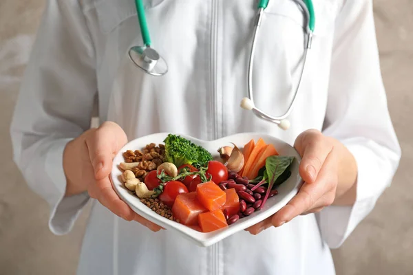 Arzt hält Teller mit Produkten für herzgesunde Ernährung, Nahaufnahme — Stockfoto