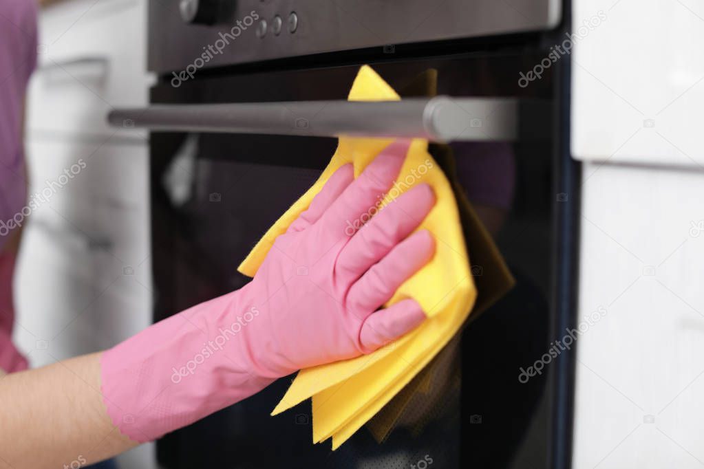 Woman cleaning oven with rag in kitchen, closeup