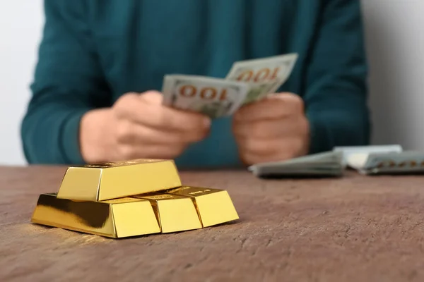 Person counting money at table, focus on stacked gold bars. Space for text
