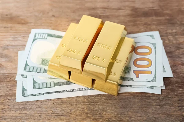 Gold bars and dollar bills on wooden table