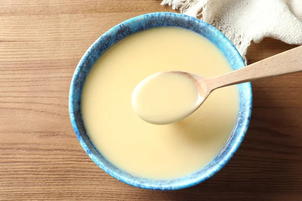 Sked och skål med kondenserad mjölk på trä bord, uppifrån. Mejeriprodukter — Stockfoto