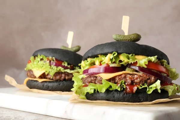 Deska s černými hamburgery na stole proti barevnému pozadí, zaostřená — Stock fotografie