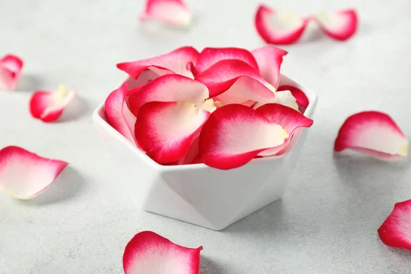Bowl with rose petals on light background