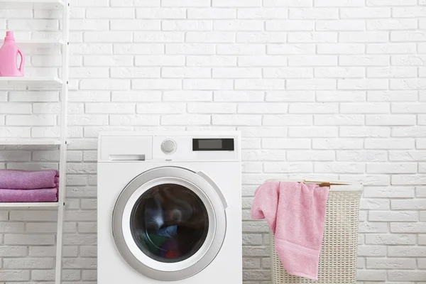 Máquina de lavar roupa moderna perto da parede de tijolo no interior da lavanderia — Fotografia de Stock