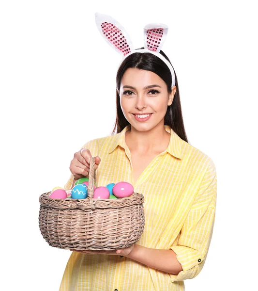 Beautiful woman in bunny ears headband holding basket with Easter eggs on white background — Stock Photo, Image