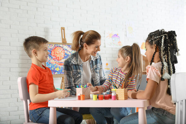 Дети с учительницей живописи на уроке живописи в помещении
