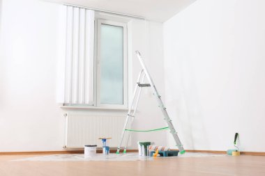 Boş odadaki duvarın yanındaki merdiven ve boya aletleri