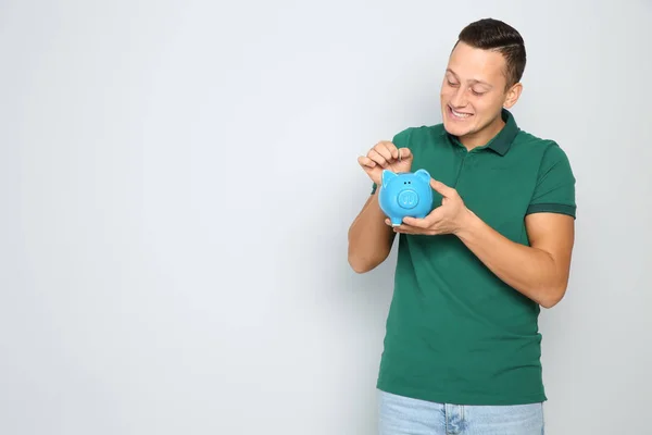 Joven poniendo moneda en alcancía sobre fondo blanco. Espacio para texto —  Fotos de Stock