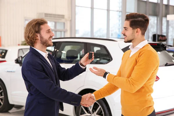 Vendedor de coches dando la llave al cliente mientras que da la mano en concesionario — Foto de Stock