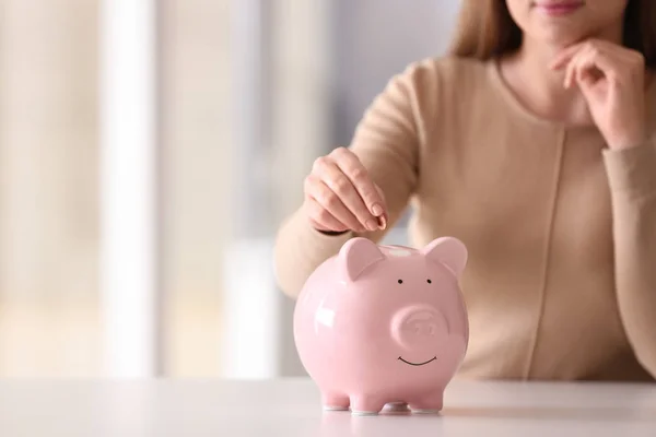 Mujer poniendo moneda en alcancía en la mesa en el interior, primer plano. Espacio para texto — Foto de Stock