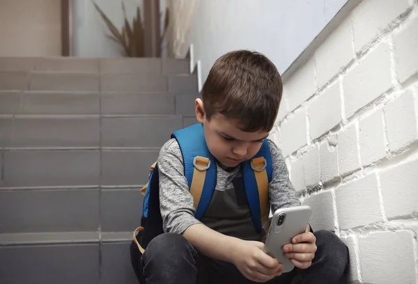 Triste petit garçon avec téléphone portable assis sur les escaliers à l'intérieur — Photo