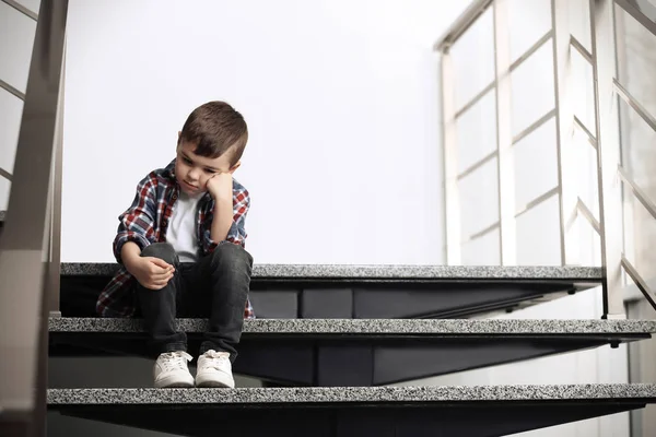 Triste petit garçon assis sur les escaliers à l'intérieur — Photo